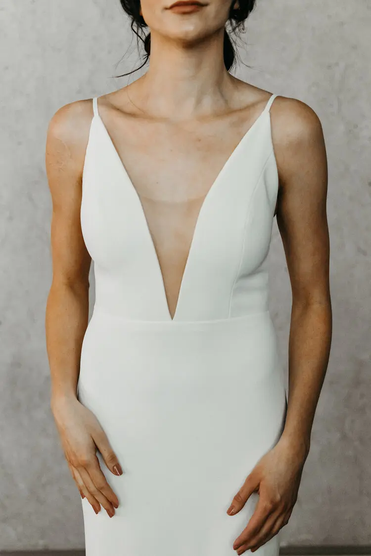 Emerson, an ivory crepe fit and flare bridal gown by Alyssa Kristin, featuring a deep V-neck illusion plunge, delicate spaghetti straps, and a low back.