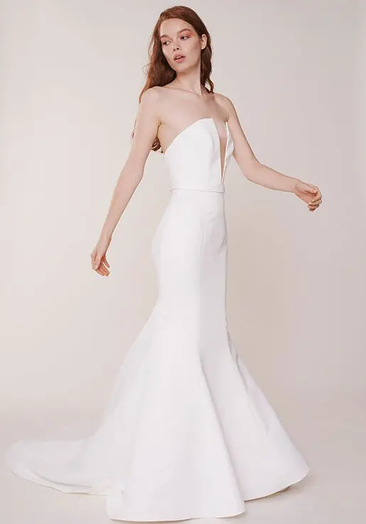 Windsor, an ivory strapless mermaid bridal gown by Alyne, featuring a deep plunge V-neckline, a fitted satin bodice, and a dramatic fit-and-flare silhouette extending into a chapel train. Available in sizes 12 and 18.