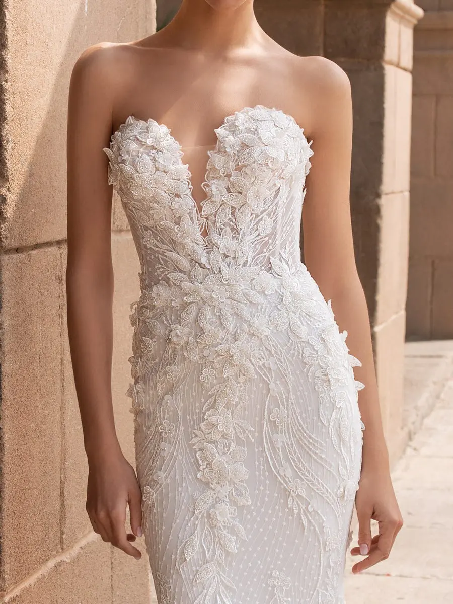 1627484778396-aethra_h_uowdjhvw8zx25qmw Aethra, an Off-White and Crystal strapless Pronovias mermaid bridal gown. The dress features a deep plunging sweetheart neckline with a sheer illusion panel, and is intricately adorned with elaborate 3D floral appliqués, beading, and delicate embroidery that densely covers the bodice and extends down the fitted skirt.