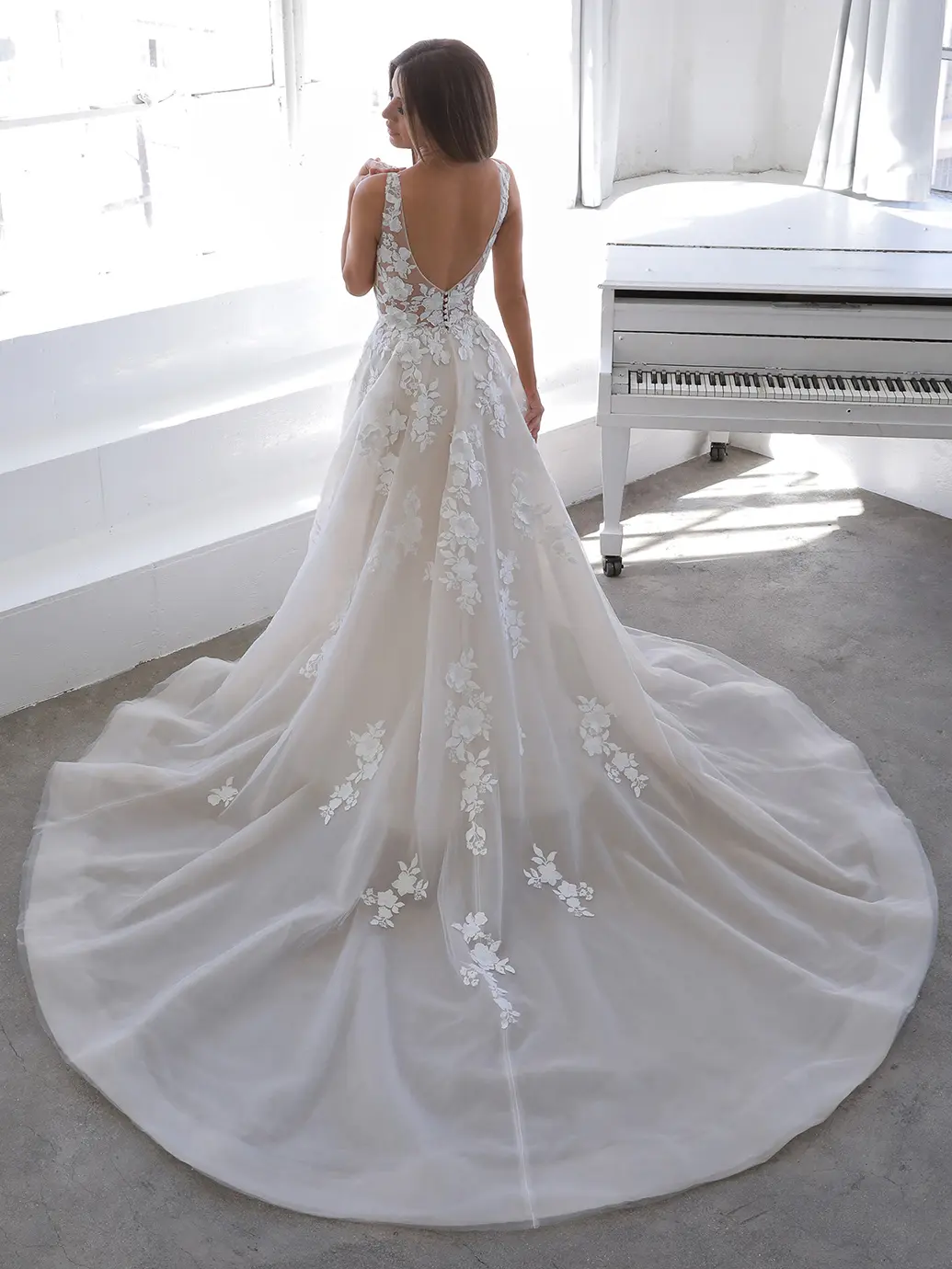 Web Nala, an ivory and nude A-line wedding gown by Blue by Enzoani, featuring a plunging V-neckline, low V-back, and delicate floral 3D appliqués meticulously scattered across the bodice and flowing organza skirt, which extends into a cathedral train.