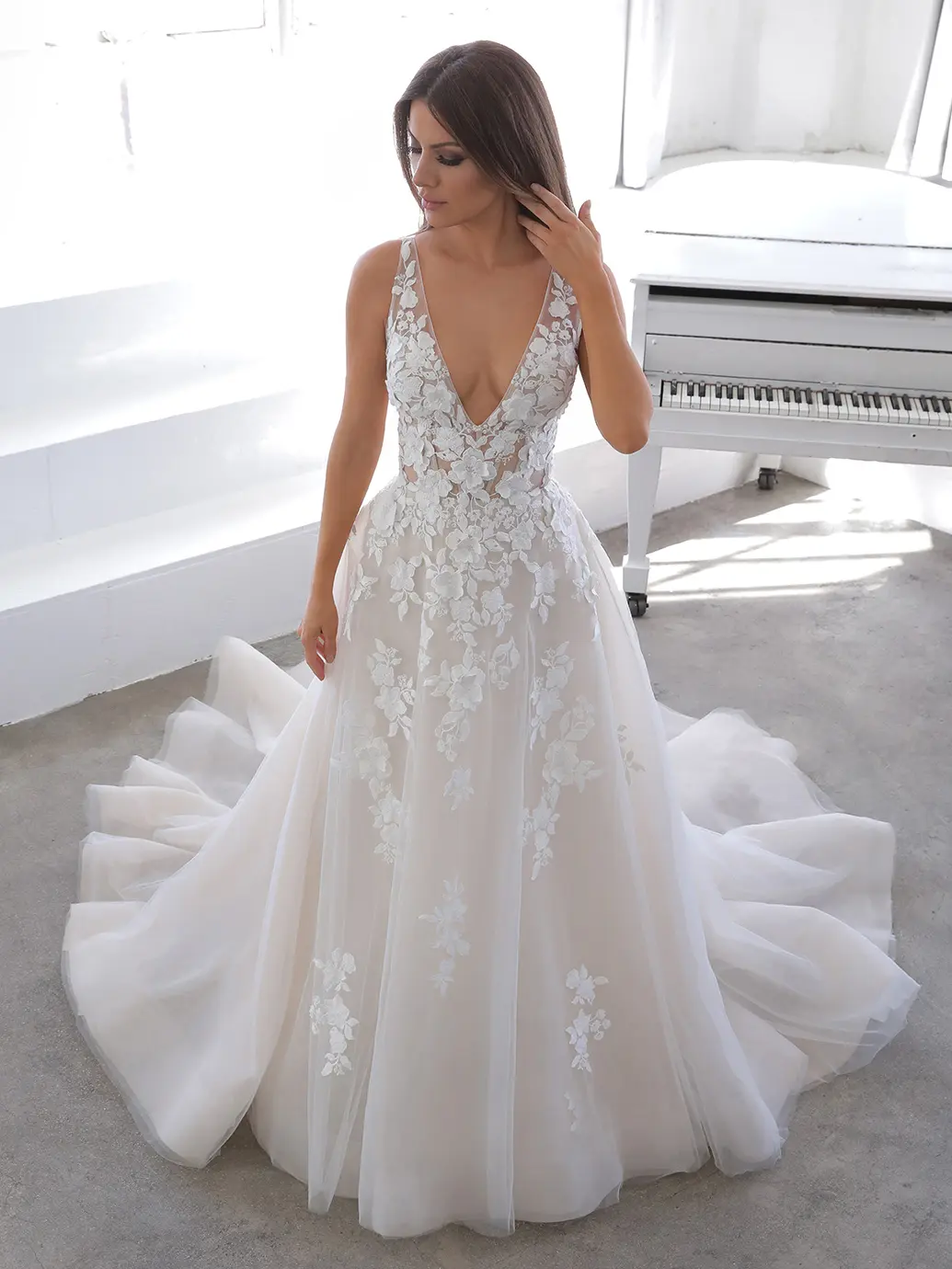 Nala, an ivory and nude A-line wedding gown featuring a deep V-neckline, intricate floral lace appliques on the sheer bodice and throughout the full tulle and organza skirt, which flows into a cathedral train.