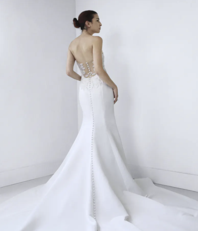 1659120300787-screen-shot-2022-07-29-at-2-44-26-pm Ady, an ivory fit-and-flare wedding gown crafted from luxurious matte satin, features a strapless sweetheart bodice with hand-appliquéd beaded lace, an illusion open back with delicate sheer fabric and lace detailing, and a row of covered buttons flowing down its dramatic train.