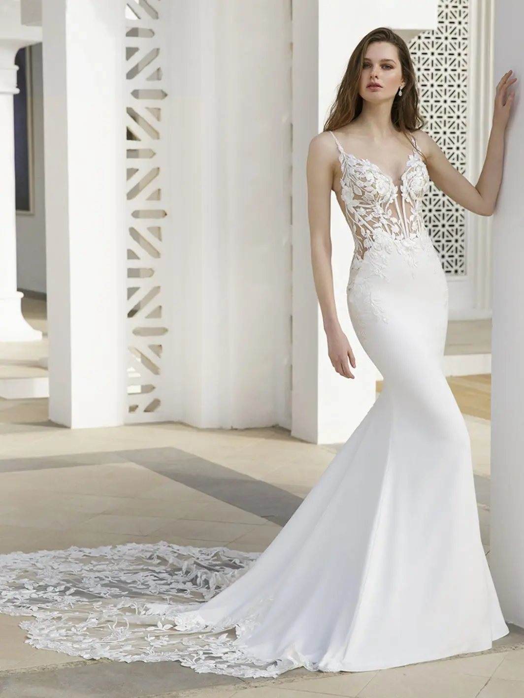 Ryder, an ivory and nude fit and flare bridal gown with a deep plunging illusion lace and beaded bodice with spaghetti straps, and a smooth crepe skirt leading to a cathedral-length lace train.