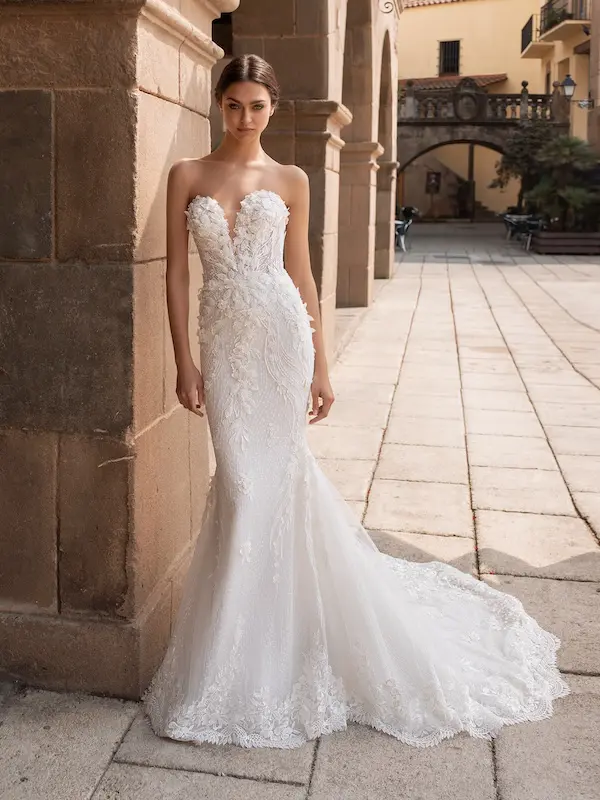Aethra, an Off White/Crystal Pronovias strapless mermaid bridal gown featuring a deep plunge sweetheart neckline, intricate lace and embroidered appliques over tulle, and a flowing chapel train.