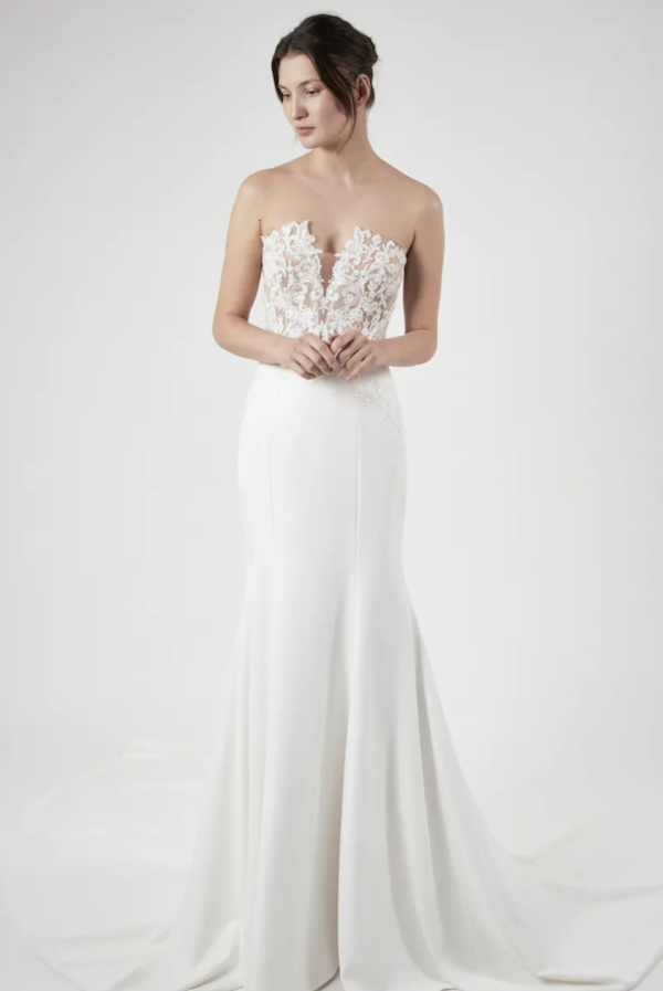 Zadye, an ivory strapless fit-and-flare bridal gown by Alyne, featuring a plunging neckline, a delicate lace bodice with intricate beading, and a smooth crepe skirt with a cathedral train, shown on a model against a white background.