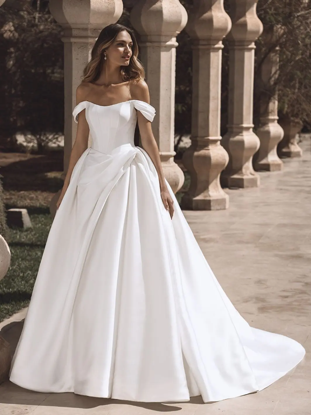 Viviana, an ivory Enzoani bridal ball gown crafted from luxurious Mikado fabric, featuring a strapless corset bodice with an off-the-shoulder scoop neckline and subtle ruching at the waist. The voluminous skirt flows into a dramatic cathedral train, detailed with buttons.