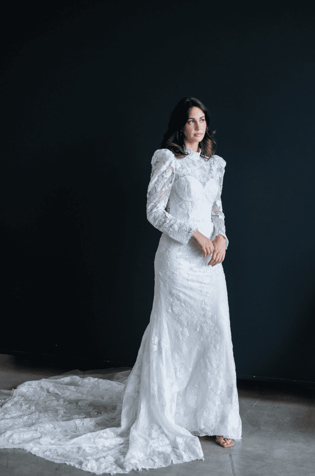1668784641967-screen-shot-2022-11-18-at-10-15-58-am-2 Macie, an ivory fit-and-flare bridal gown crafted from intricate lace, featuring a high neckline, long sleeves with soft shoulder puffs, and a sweeping cathedral train.