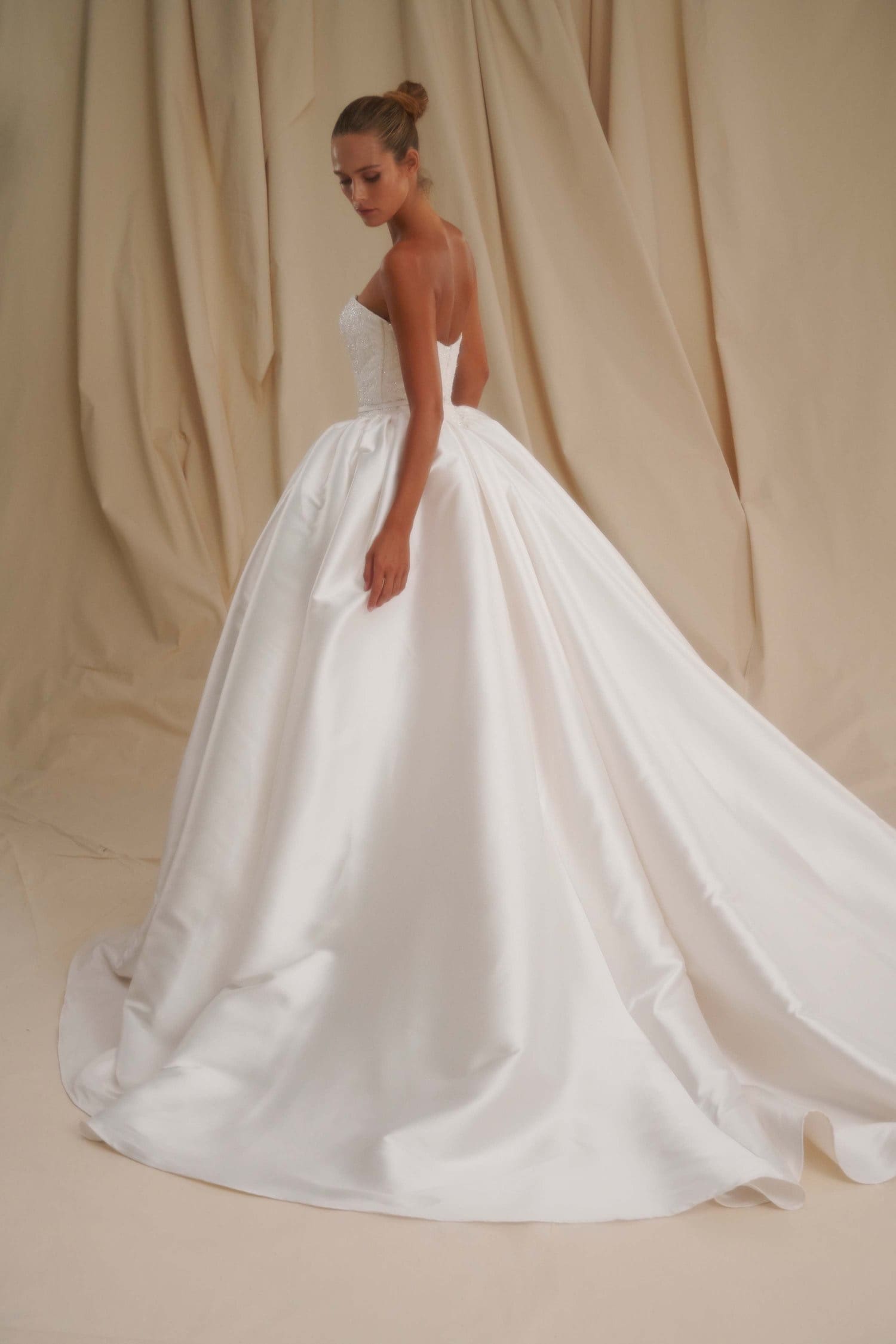 1729784588227-image-16-2 SE001 by Senstudio, a Diamond White strapless ball gown, featuring a delicate lace and sequin bodice, a flattering Basque waist, and a lustrous mikado skirt with a cathedral train, shown on a model from the back and side.