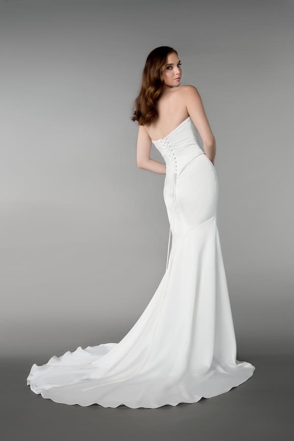 1740172944727-RNG_55233_FB-5 An ivory charmeuse fit-and-flare bridal gown by Adorn Nashville. The strapless dress features a sweetheart neckline, a ruched and draped bodice, and a lace-up corset back with a modesty panel. A chapel-length train flows behind the model, who is looking over her left shoulder from the back.