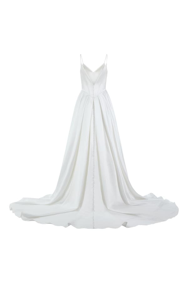 1740173332638-rng-55234lnd-fb Lucy, an ivory A-line satin bridal gown with delicate spaghetti straps and a V-neckline. The back view reveals a sophisticated V-back adorned with a cascade of buttons running down to the end of its chapel-length train. It features a basque waistline and a voluminous pleated skirt, complete with hidden pockets.