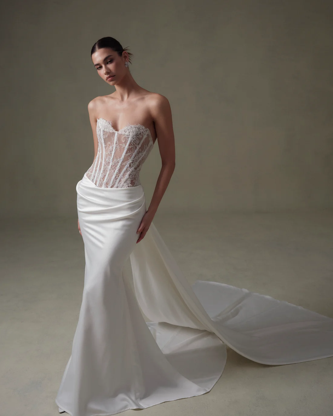 1745435042283-20250313NF4794 A Senstudio ivory and nude strapless mermaid wedding gown featuring a sculpted sheer lace corset bodice with delicate floral embroidery and visible boning, complemented by a sleek, draped satin skirt that dramatically flares into a sweeping panel train.