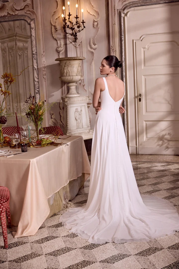 1747243408733-88473_Lupita_FB_Justin-Alexander_5 Lupita, an ivory A-line bridal gown featuring a sleek crepe bodice with a modern scoop neckline, an inset basque waist, and a lightweight chiffon skirt flowing into a chapel-length train with a full button-down back.