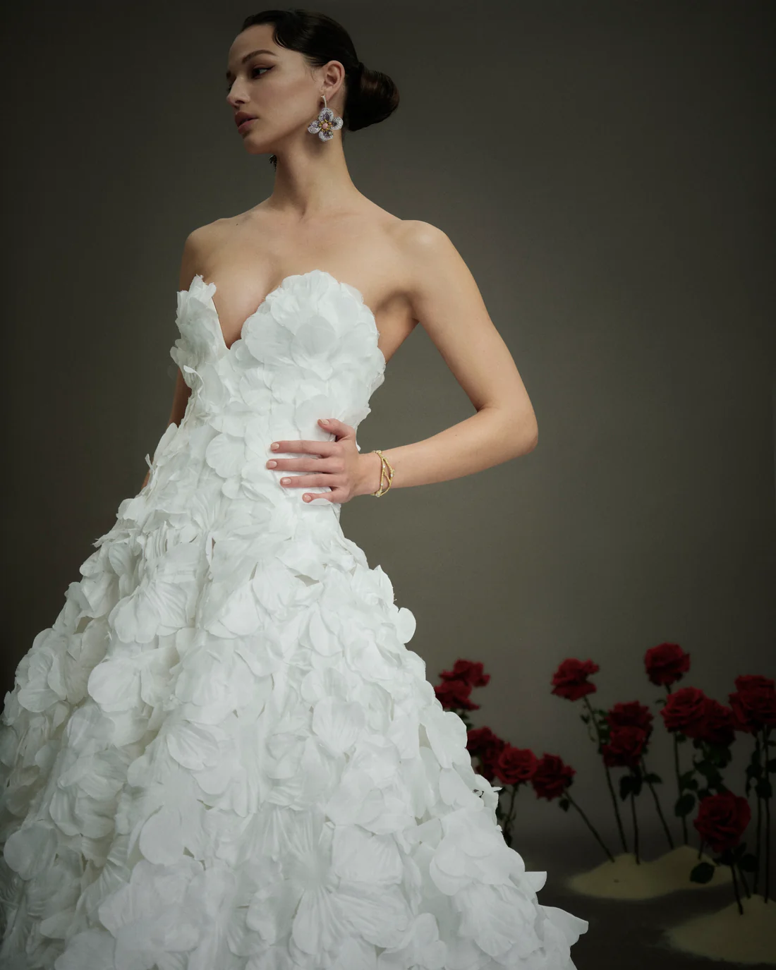 1748022927679-NF1959 A model wears the NF114, a light ivory strapless V-neck ballgown featuring delicate, layered 3D floral petals cascading throughout its full, voluminous skirt and a dramatic cathedral-length train.