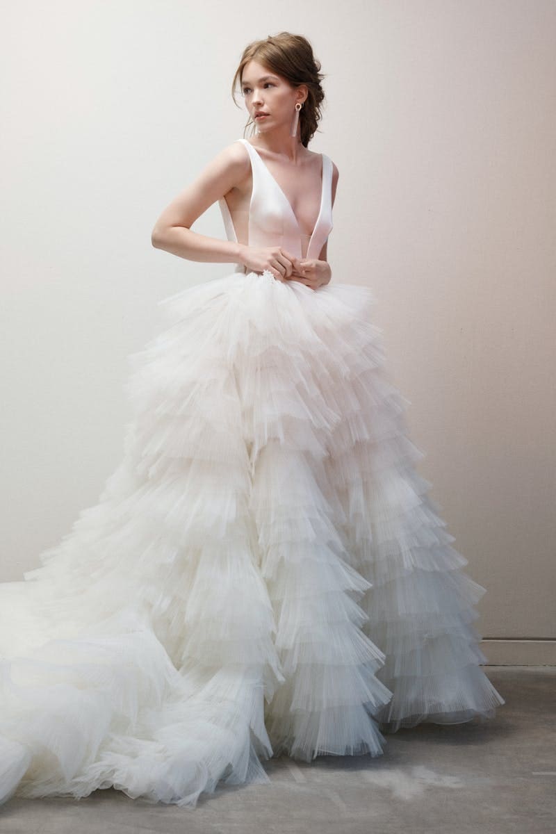 1646854161751-rivini-sleeveless-v-neck-textured-ball-gown-wedding-dress-34340034 Ross, an ivory wedding gown featuring a plunging V-neck bodice, a low back, and a voluminous ball gown skirt created from dramatic tiers of ruffled tulle, extending into a cathedral train.