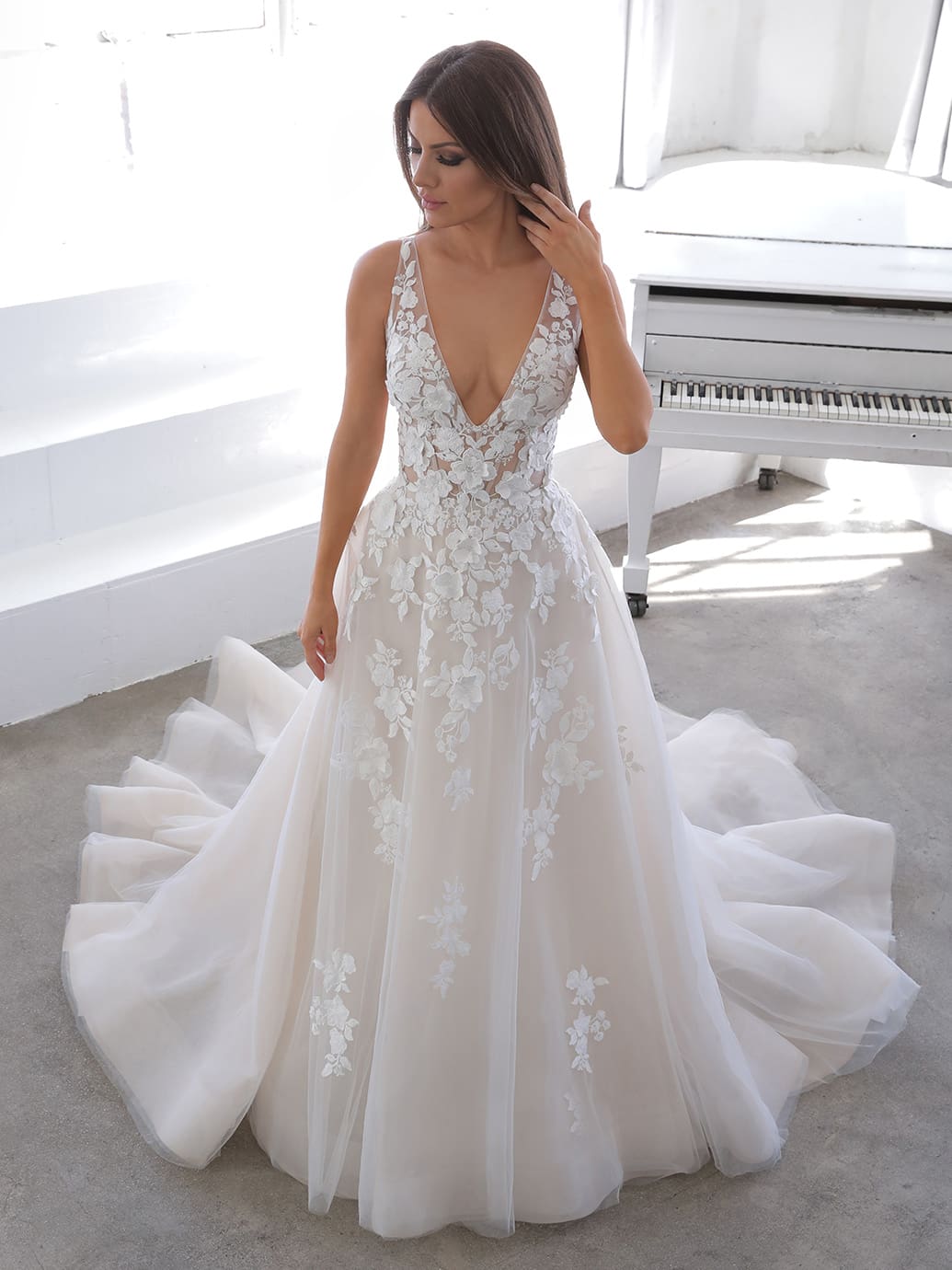 Web Nala, an ivory and nude A-line wedding gown featuring a deep V-neckline, intricate floral lace appliques on the sheer bodice and throughout the full tulle and organza skirt, which flows into a cathedral train.