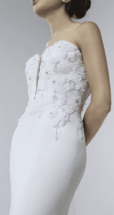 Ady, an ivory Alyne bridal gown featuring a strapless sweetheart neckline with a subtle plunge, a corset bodice adorned with intricate lace, beading, and floral applique, and a smooth satin mermaid skirt.