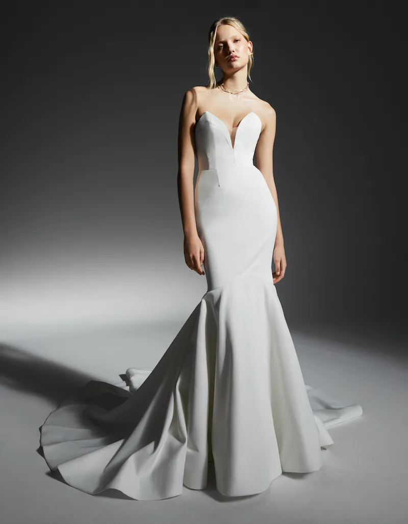 Hanna, an ivory strapless mermaid wedding gown with a sweetheart plunge V-neckline and illusion detail, crafted from satin, featuring a dramatic cathedral train, worn by a blonde model in a studio setting.