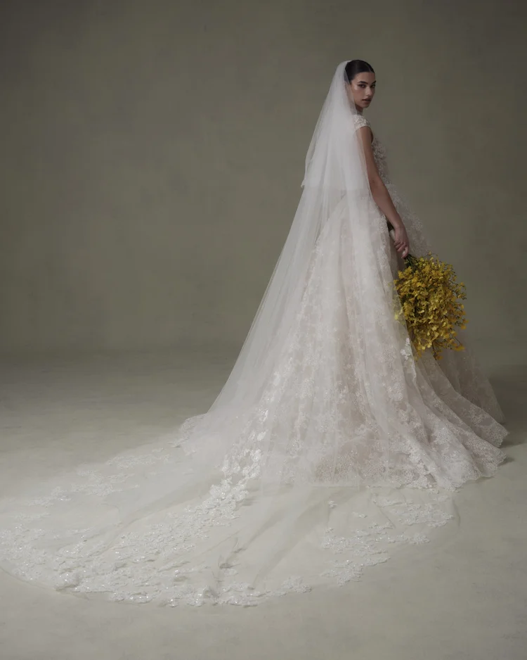 1762970232881-2025-0313-NF4291 SE093 Privee, an Ivory/Nude bridal ball gown featuring a high neckline, delicate cap sleeves, and a full skirt adorned with intricately beaded lace that shimmers subtly. A sweeping chapel-length train completes this elegant and romantic look.